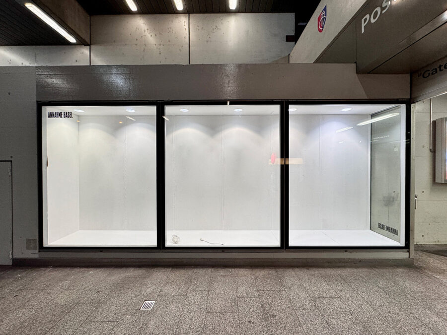 Three empty, brightly lit white display windows in a concrete building.