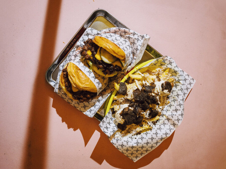 Two burgers and a side of loaded fries on a metal tray with branded parchment paper.