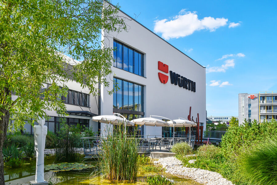 Modern white Würth office building with a landscaped garden and pond in the foreground.