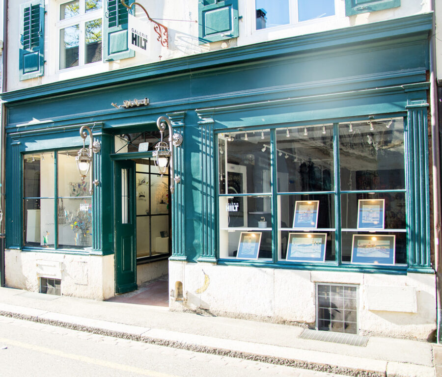 The exterior of Galerie Hilt, an art gallery with a dark green storefront and large display windows.