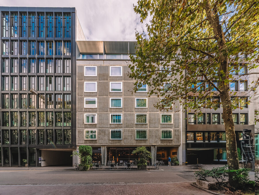 Modern office buildings of varying architectural styles next to a large leafy tree.