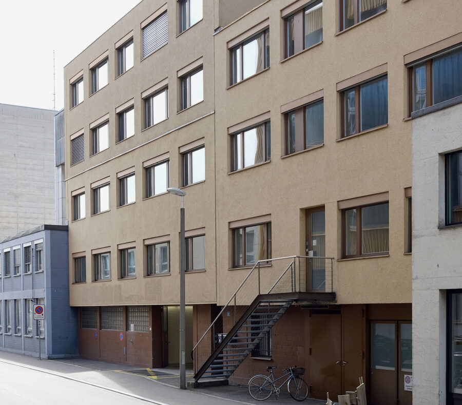 A multi-story beige office building with rows of windows and an external metal staircase.