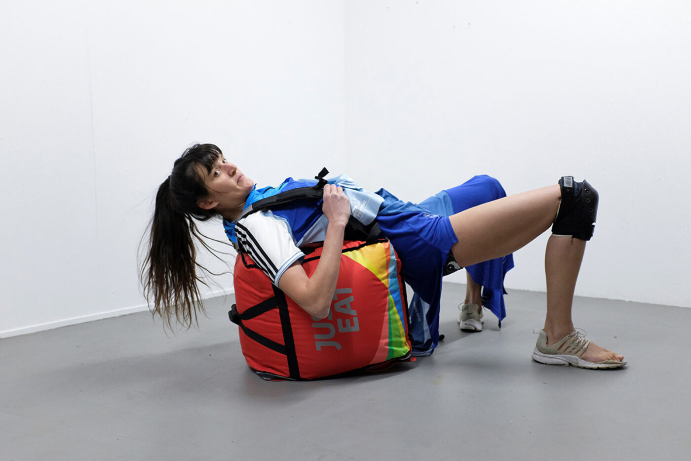 Eine Person in Sportkleidung liegt mit einer roten Just Eat-Liefertasche in einem weißen Raum.