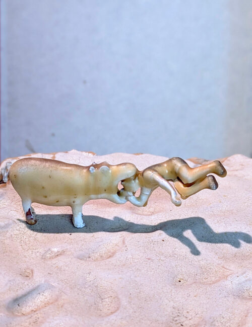 Eine kleine, beige Keramikfigur eines tierähnlichen Wesens, das eine menschliche Figur trägt.