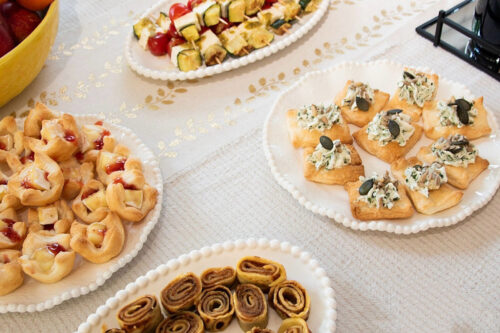 Verschiedene Platten mit herzhaften und süßen Fingerfood-Häppchen auf einer weißen Tischdecke.