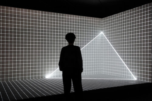 Silhouette einer Person vor einer leuchtenden Gitterwand mit einem Lichtdreieck.