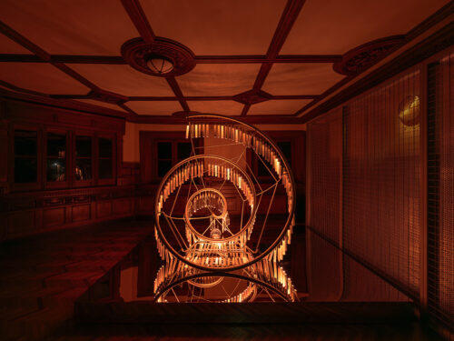 Eine spiralförmige, golden leuchtende Skulptur in einem dunkelroten, holzgetäfelten Raum.