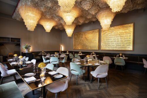 Ein luxuriöses Restaurant mit hellen Designerstühlen und einer skulpturalen, goldleuchtenden Decke.