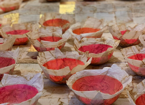 Viele kleine, rote Schalen aus zerknittertem Papier auf einem hellen Untergrund.