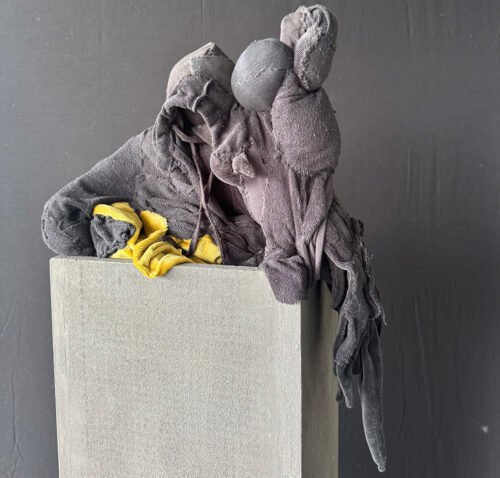 Eine abstrakte Skulptur aus grauem und gelbem Stoff auf einem grauen Betonsockel.