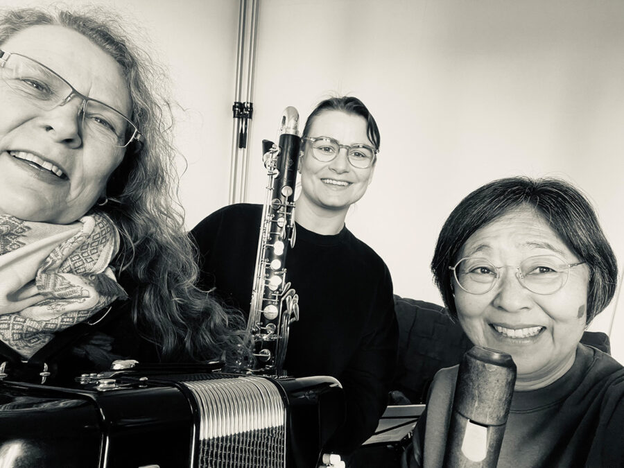 Black and white photo of three smiling women with a concertina and a bass clarinet.