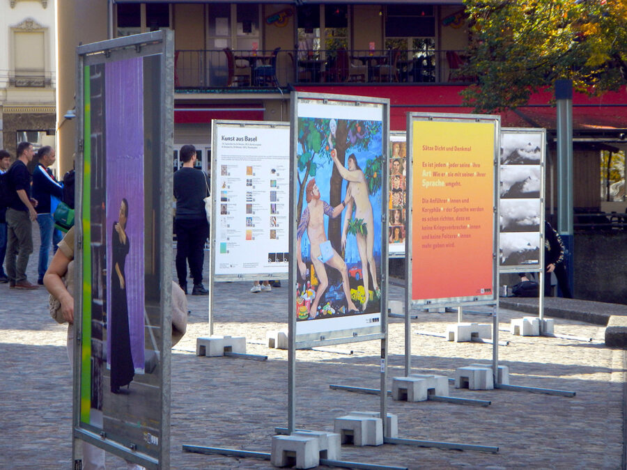 Eine Reihe von Informationstafeln mit Kunstwerken und Texten auf einem öffentlichen Platz.