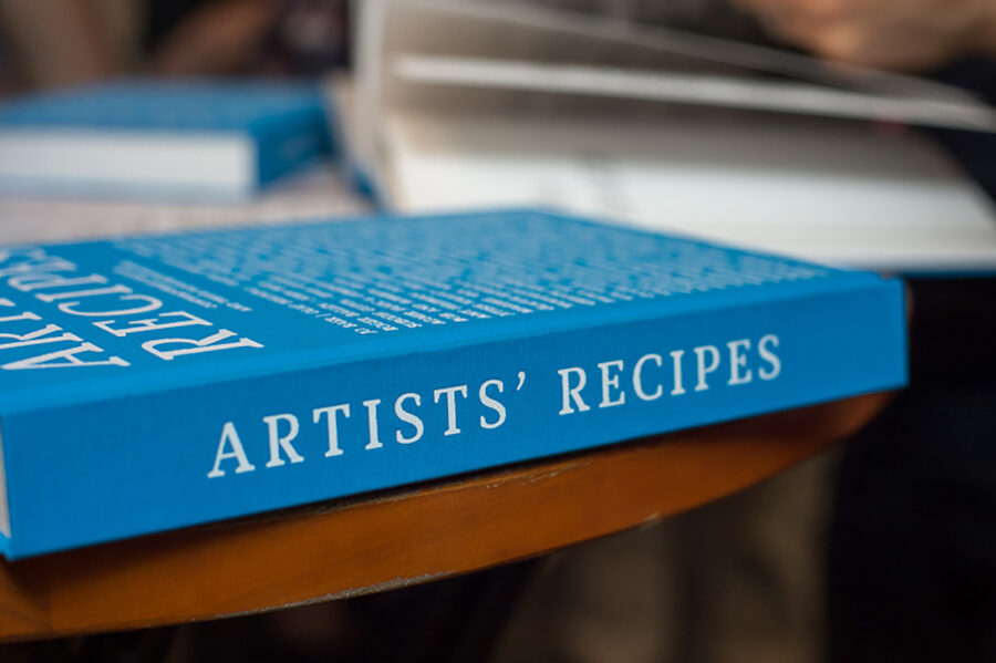 Close-up of a bright blue book titled "ARTISTS' RECIPES" resting on a wooden table.