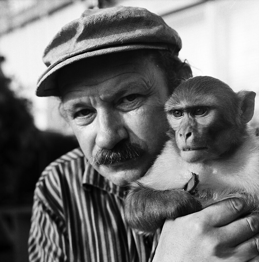 Black and white portrait of a man with a mustache and cap holding a small monkey.