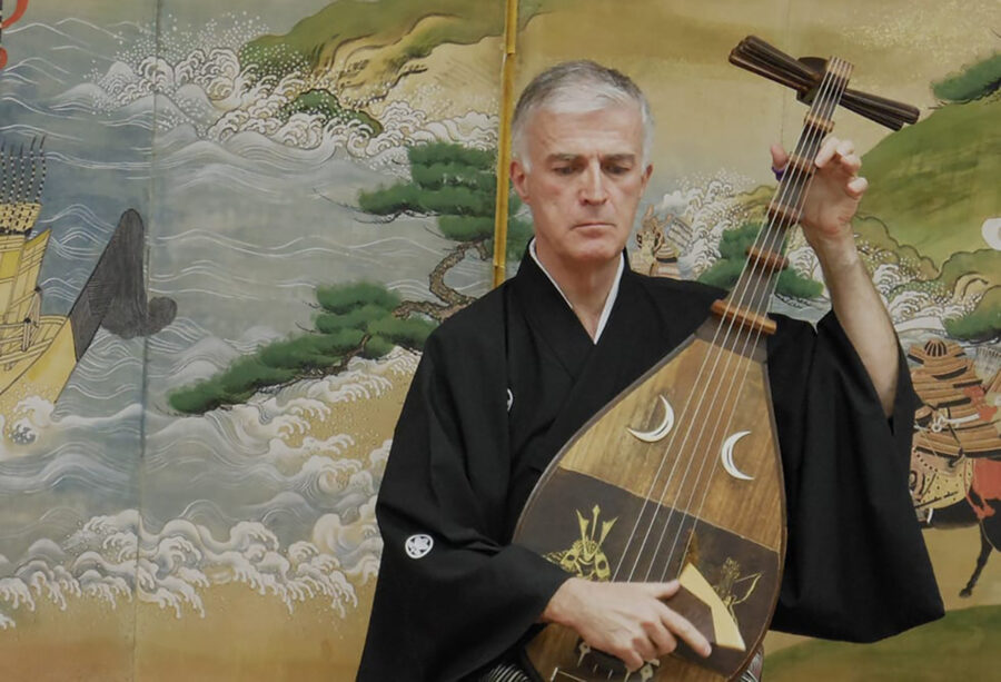Ein Mann in einem schwarzen Kimono spielt eine traditionelle japanische Biwa-Laute.