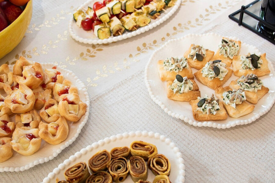 Verschiedene Platten mit herzhaften und süßen Fingerfood-Häppchen auf einer weißen Tischdecke.