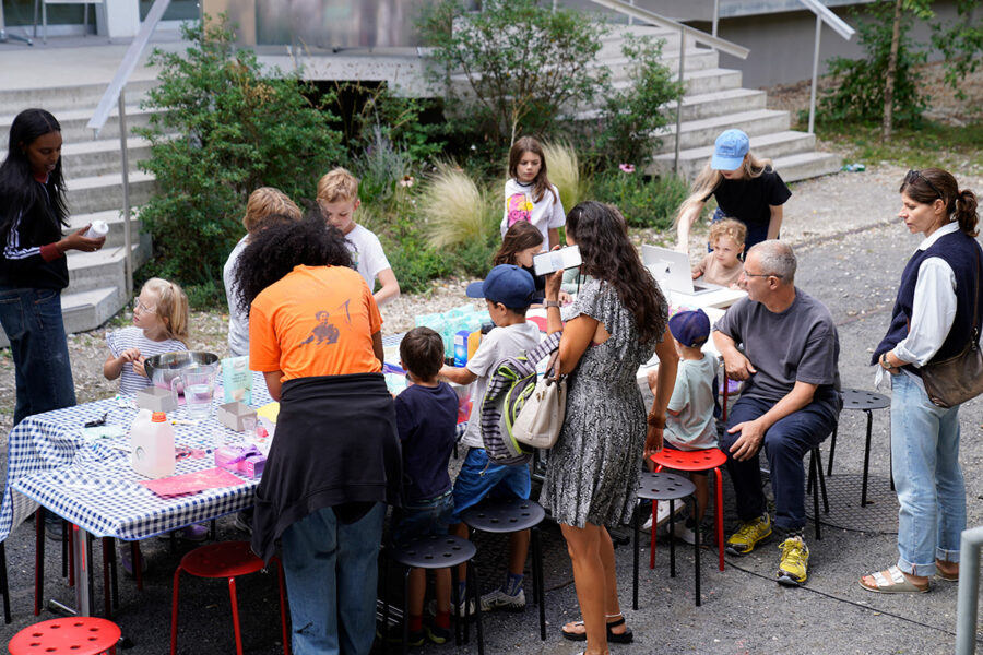 Eine Gruppe von Erwachsenen und Kindern bei einer gemeinsamen Aktivität an einem Tisch im Freien.