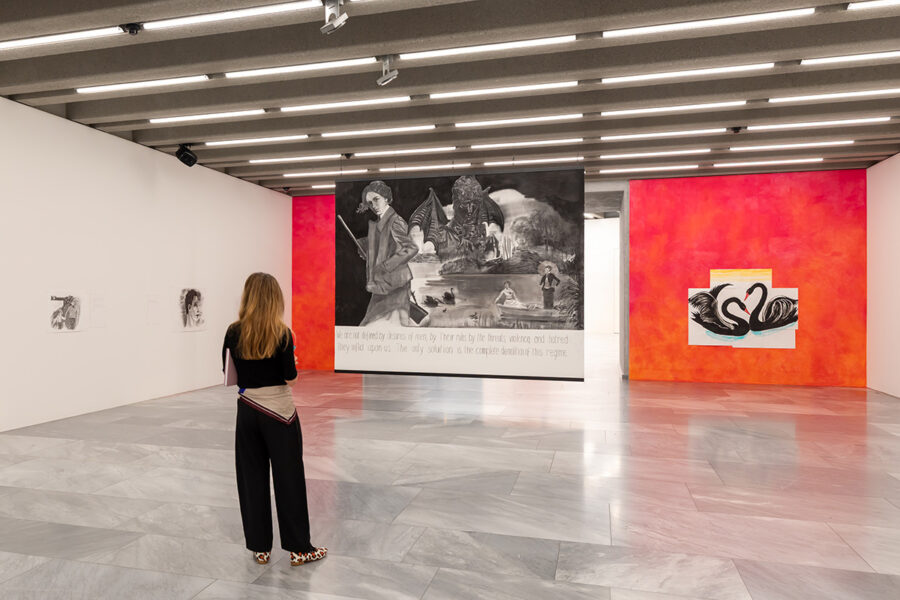 Eine Frau betrachtet in einer hellen Galerie ein großes, dunkles Gemälde mit surrealen Motiven.