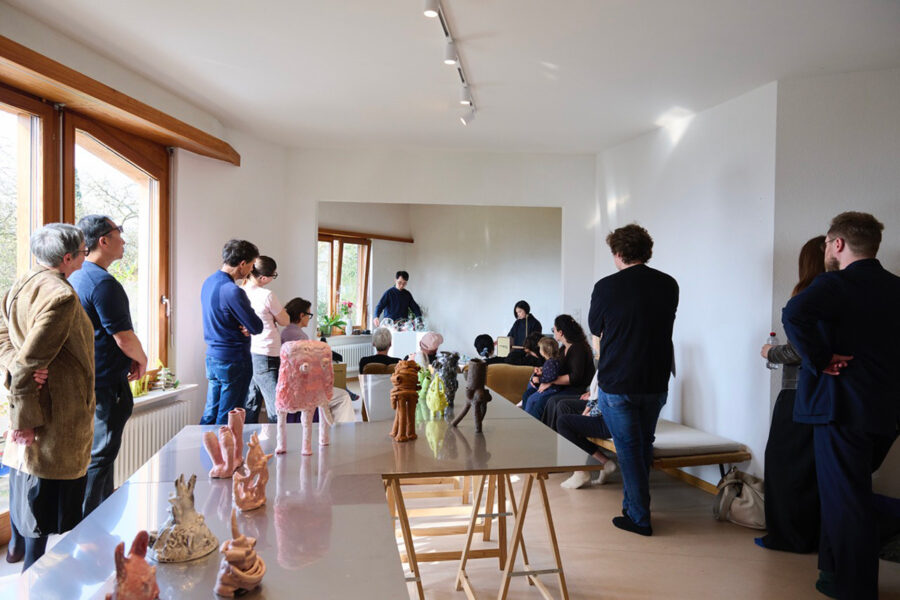 A group of people gather in a bright room to view various ceramic sculptures on tables.