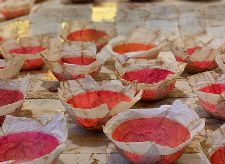 Many small, red-colored bowls lined with white parchment paper on a textured white surface.
