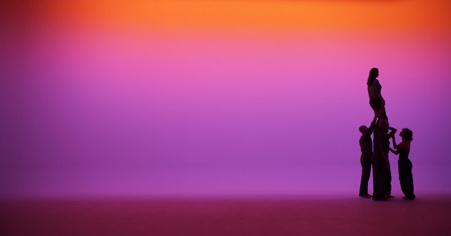Silhouetten von vier Personen vor einem violett-orangefarbenen Hintergrund.