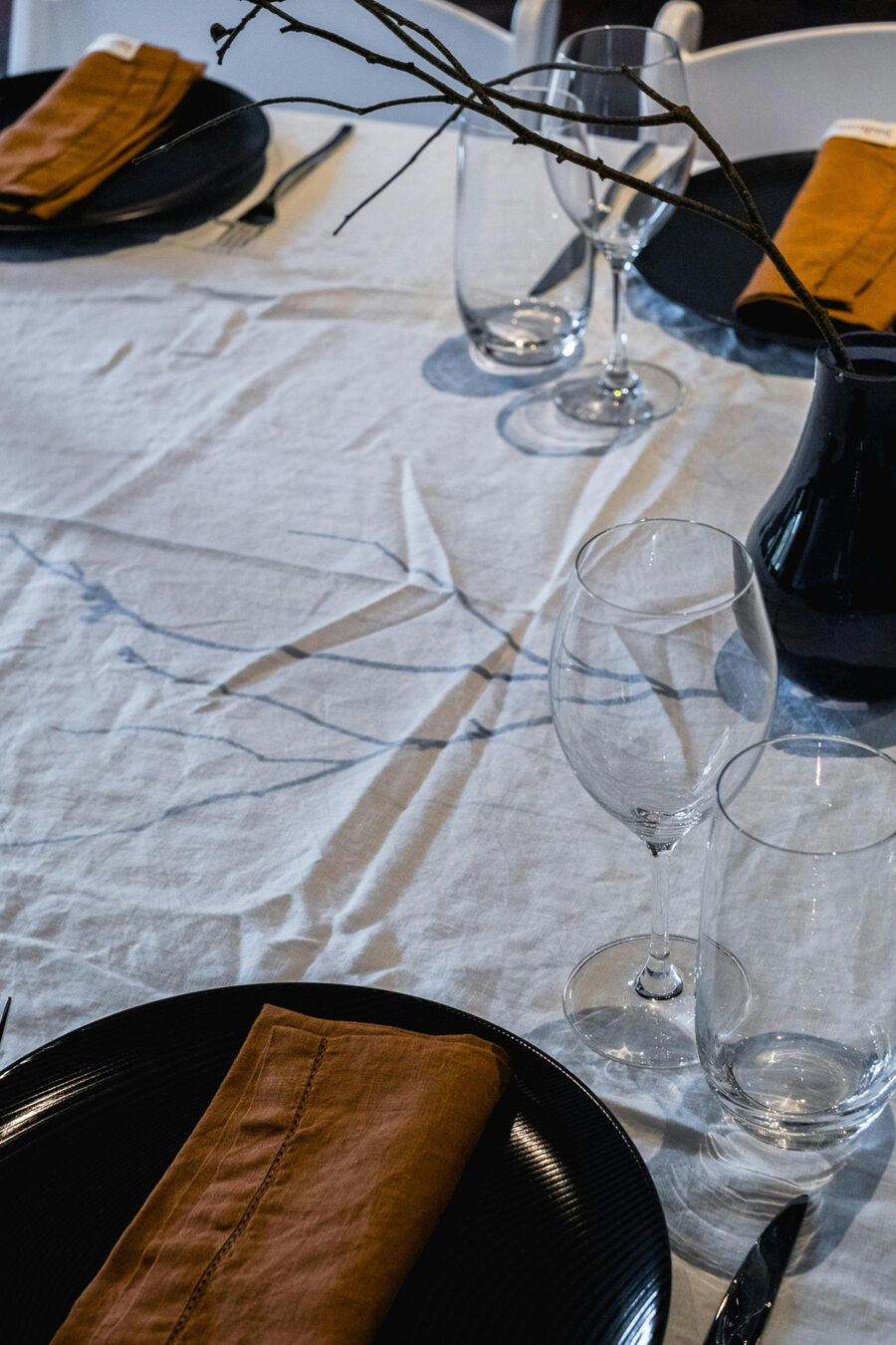 Ein festlich gedeckter Tisch mit weißem Tischtuch, schwarzen Tellern und senfgelben Servietten.