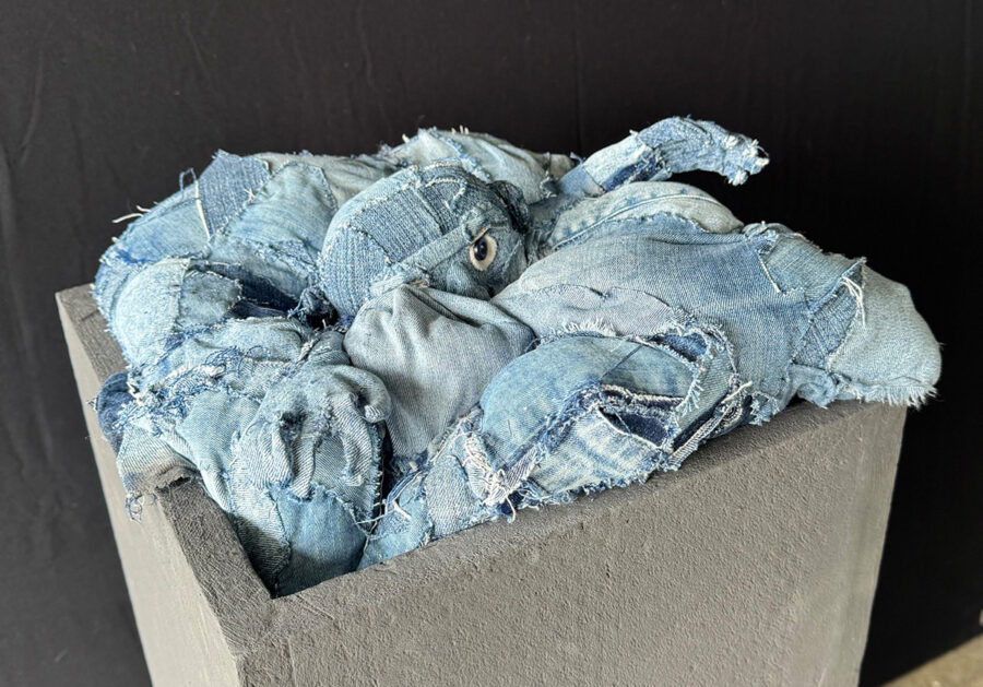 Eine aus blauen Jeansstoffresten genähte Skulptur, die aus einem grauen Kasten ragt.