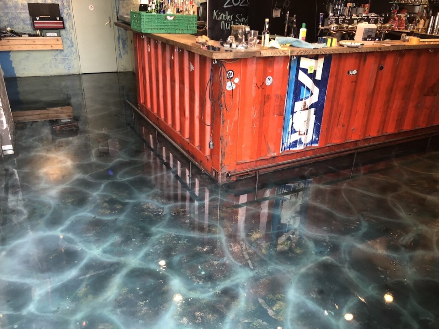 An orange shipping container bar stands on a glossy floor with a blue aquatic pattern.