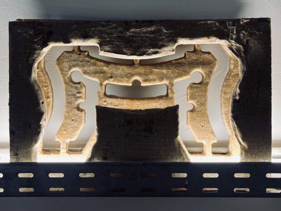 Ein rechteckiges, braunes Relief mit rissiger Oberfläche und geschwungenen, hellen Aussparungen.