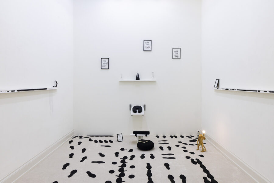 Eine minimalistische Kunstinstallation in einem weißen Raum mit schwarzen Fußabdrücken am Boden.