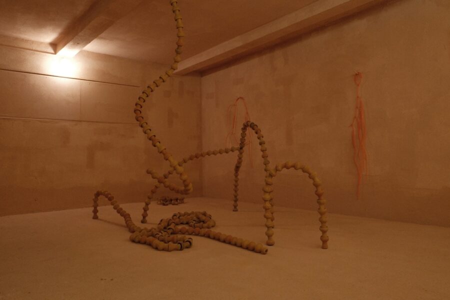 Eine Installation aus kettenartig aneinandergereihten, hellen Kerikperlen in einem leeren Raum.
