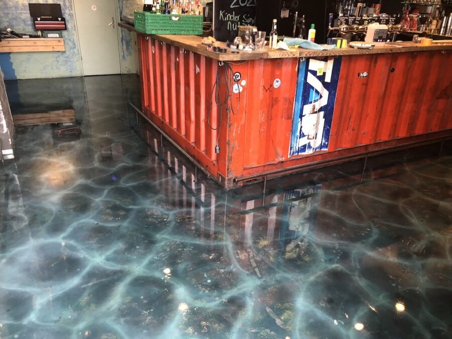 Eine rote Bar aus einem Frachtcontainer auf einem glänzenden Boden mit Wasser-Optik.