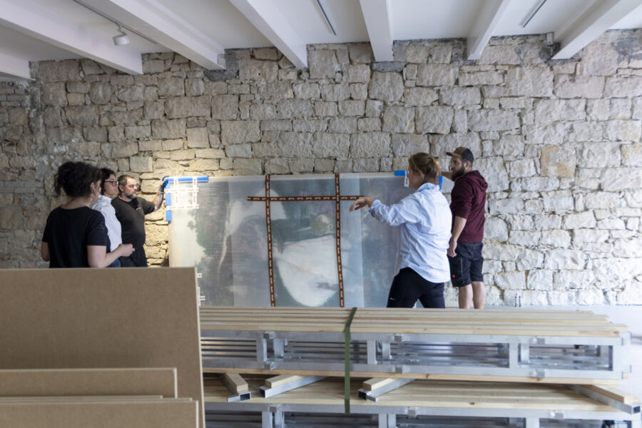 Eine Gruppe von Personen bespricht ein großes, transparentes Bild vor einer Natursteinwand.