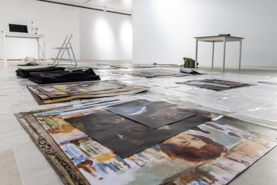 Ein heller Kunstraum mit großformatigen Drucken und schwarzen Stoffen auf dem Boden.