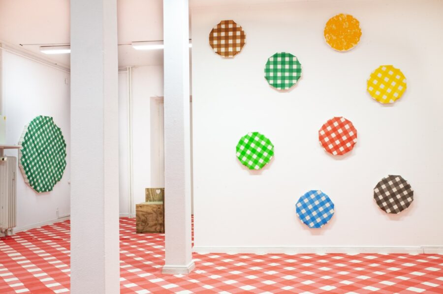 Bunte, karierte Kreise an einer weißen Wand über einem rot-weiß karierten Boden.