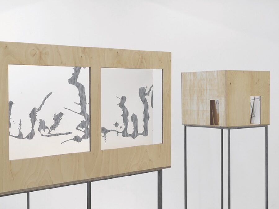 Moderne Kunstinstallation mit zwei gerahmten abstrakten Grafiken und einem Holzwürfel auf Gestellen.