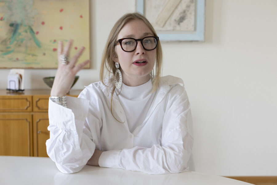 Eine Frau mit Brille und weißem Hemd gestikuliert an einem Tisch.