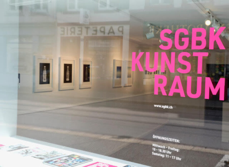 Storefront window of SGBK Kunst Raum gallery with framed art inside and pink lettering on the glass.