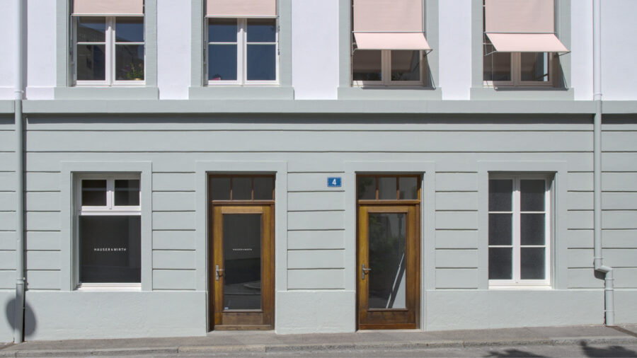 Front view of a light grey building facade with two wooden doors and several windows.