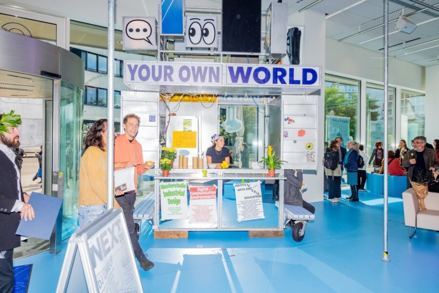 People gathered around a creative pop-up booth labeled "YOUR OWN WORLD" in a bright blue room.