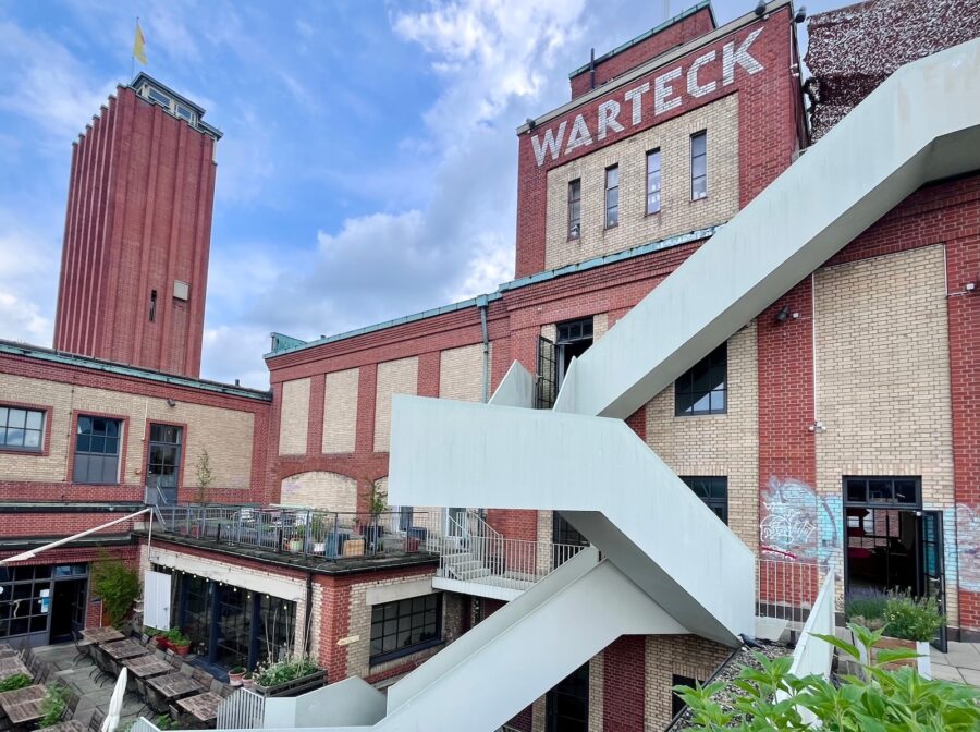 Industrial red brick buildings with a tall tower, a modern white staircase, and WARTECK signage.