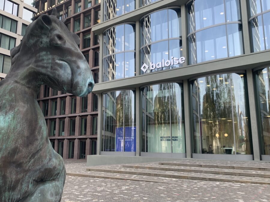 Bronze horse sculpture in the foreground with a modern Baloise office building in the background.