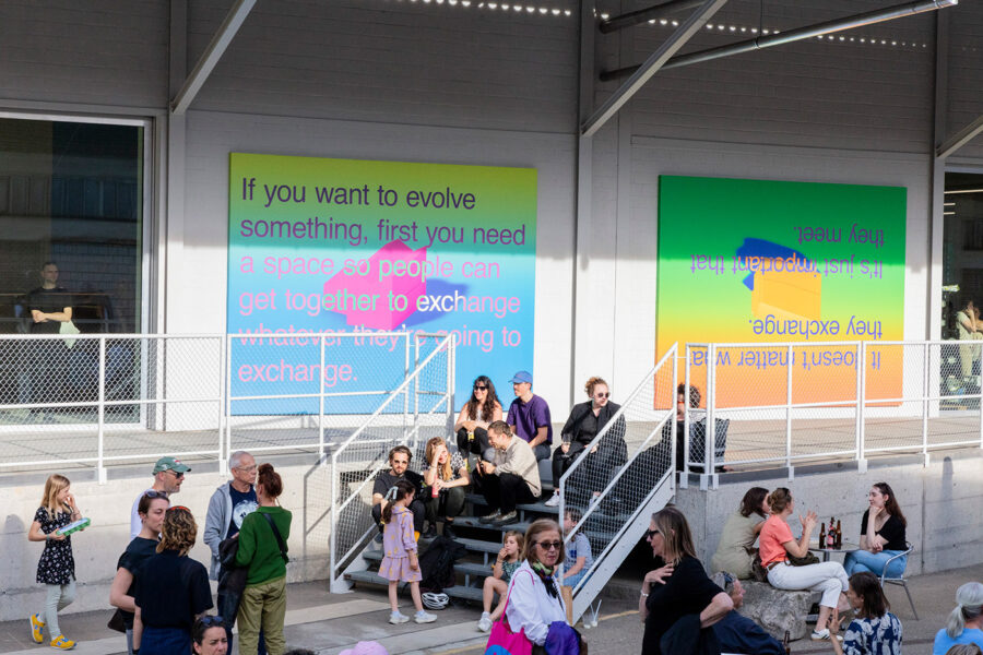 People gather outside a building featuring two large, colorful murals with text.