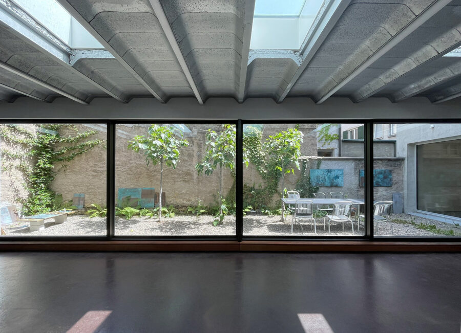 Interior view of a room with a concrete ceiling and a large window looking onto a garden patio.
