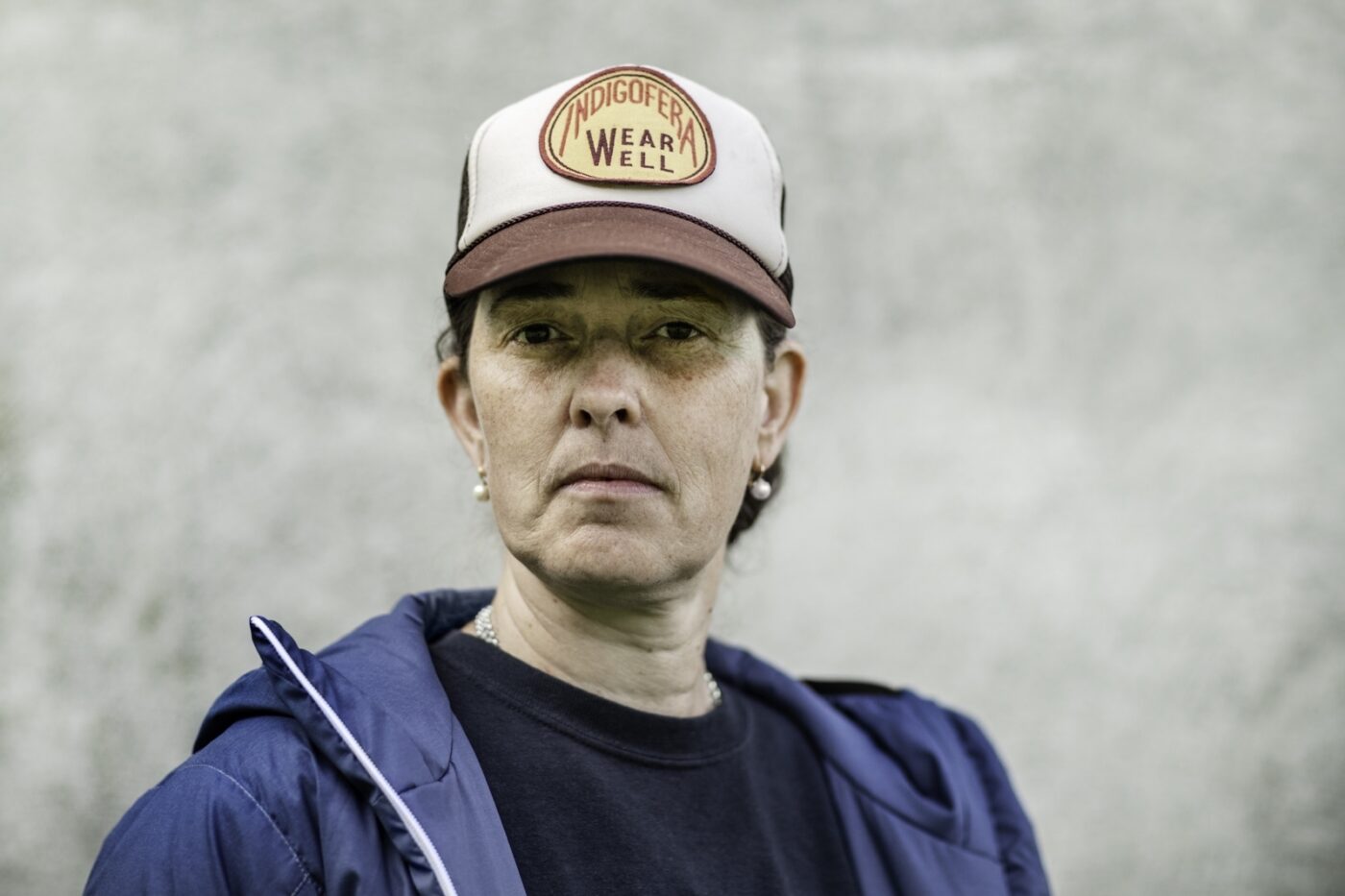 Portrait of a woman wearing a blue jacket and a cream and brown baseball cap.