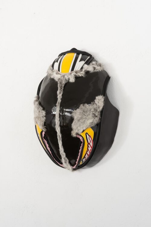 Ein schwarzer, glänzender Helm mit grauem Kunstfell und gelben Akzenten vor weißem Hintergrund.