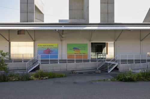 Modern building facade with two colorful text panels and stairs leading to an entrance.