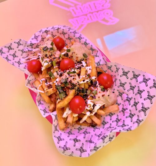 Loaded french fries topped with cherry tomatoes and sauce in a branded paper liner.