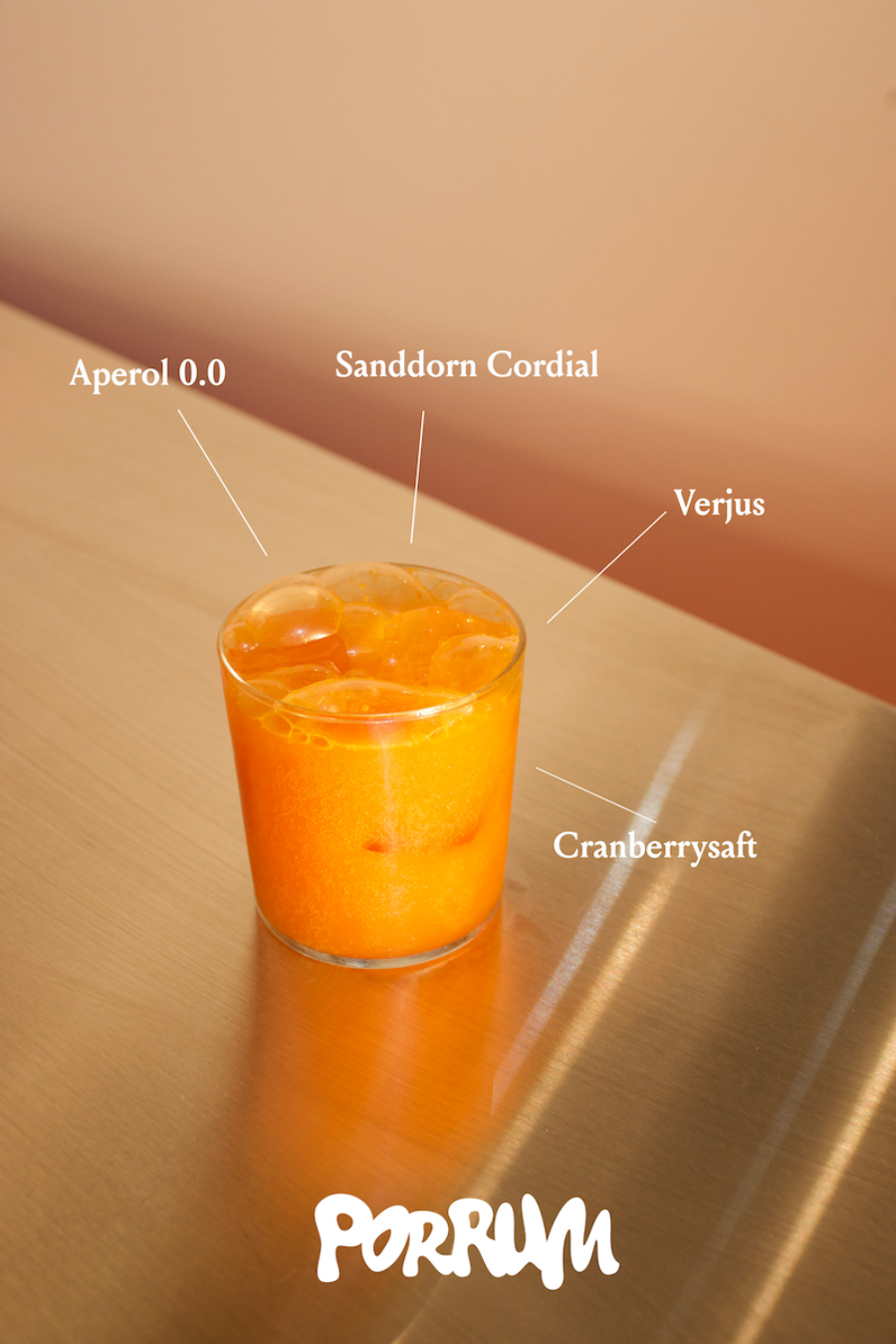 Orange cocktail with ice, labeled with ingredients: Aperol 0.0, Sanddorn Cordial, Verjus and Cranberry.