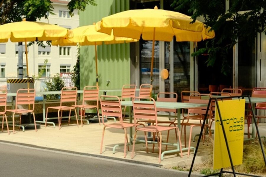 Outdoor cafe seating with pink metal chairs, mint green tables, and bright yellow umbrellas.